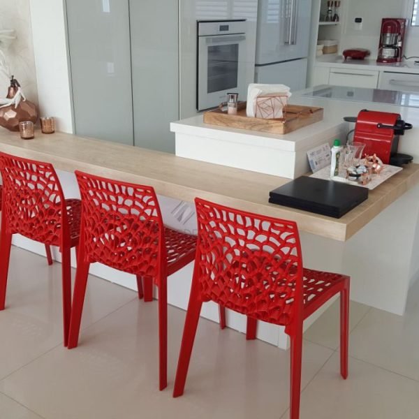 Cozinha em tons neutros, com eletrodomésticos brancos. As cadeiras vermelhas criam o elemento de destaque.